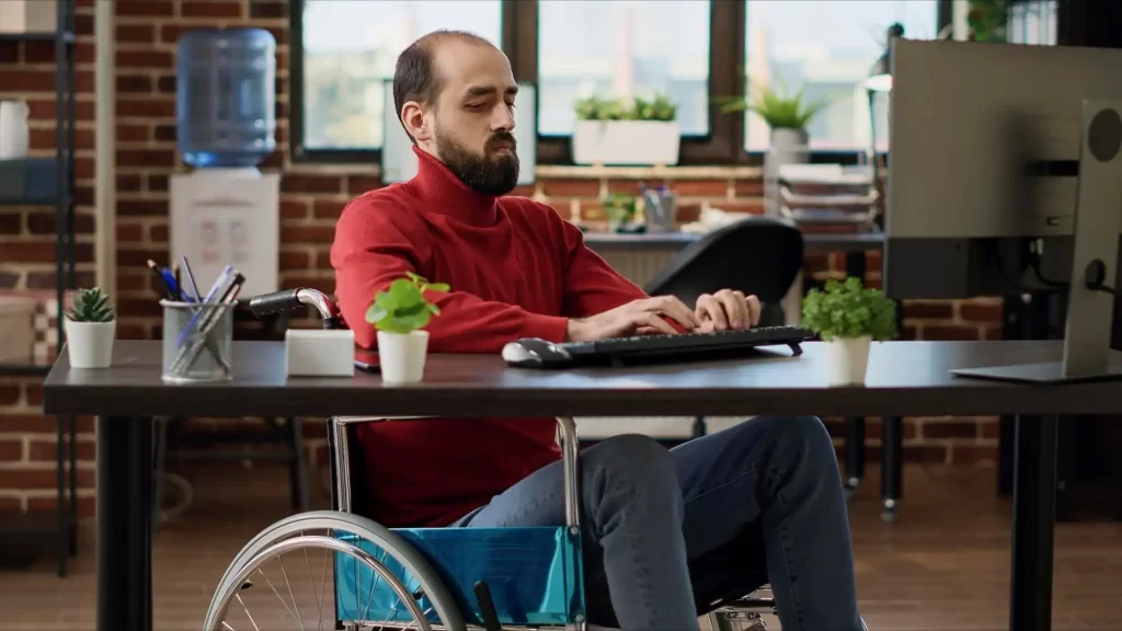 אדם בכסא גלגלים מקליד במקלדת מול מסך מחשב